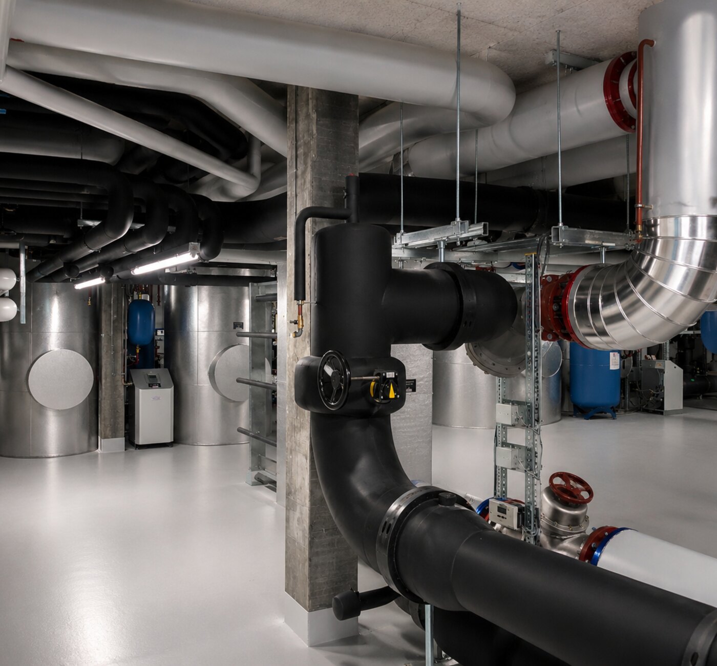Photographie du sous-sol technique une fois l’installation réalisée : collecteurs chaud et froid, bouteille de découplage et réseaux hydrauliques.